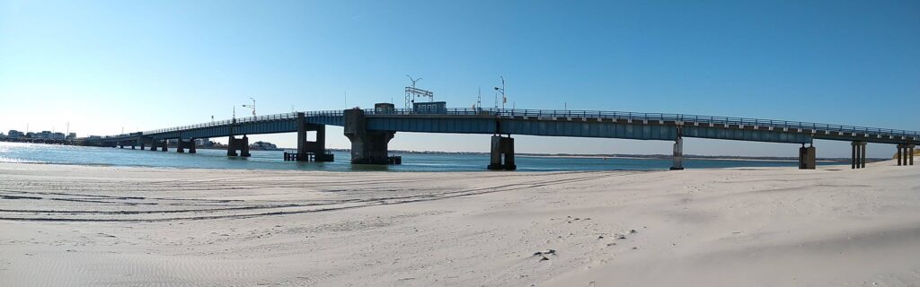 Ancient stone bridge arches over a calm river, surrounded by lush greenery and clear skies.
